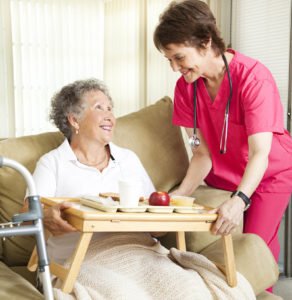 nurse serving elderly woman lunch on couch
